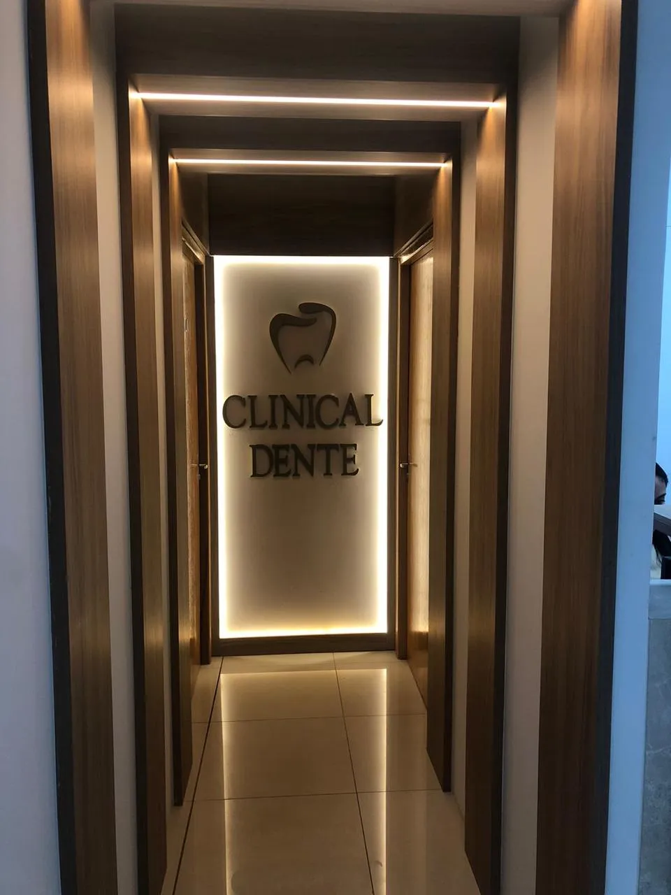 Corredor revestido de madeira com iluminação indireta no teto, que leva às salas de atendimento